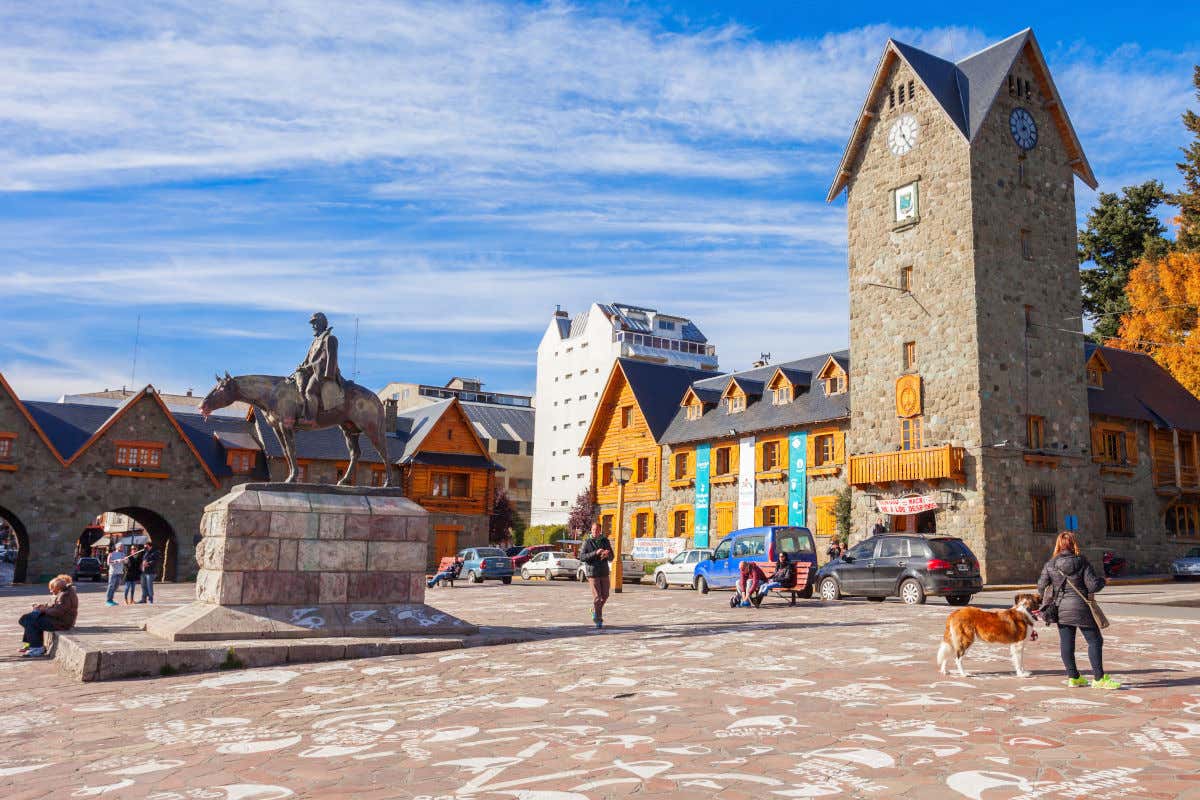 Centro Cívico de Bariloche, declarado Monumento Histórico Nacional, em frente a uma praça com várias pessoas caminhando ou sentadas