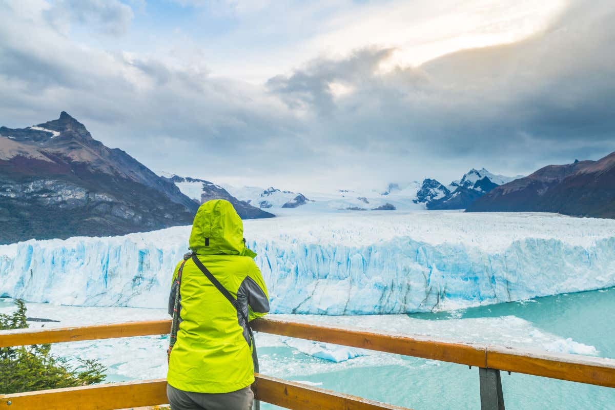 Uma mulher com roupa de inverno e cores refletivas de costas em um dos mirantes do glaciar Perito Moreno