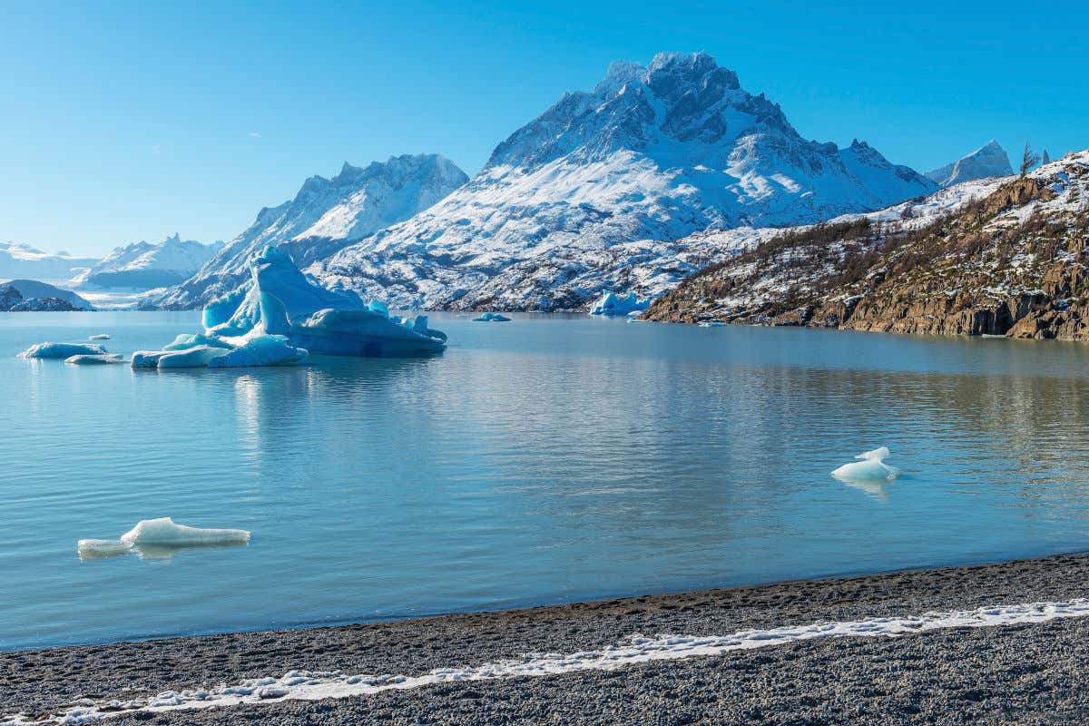 Um lago glaciar, com gelo na sua parte central e rodeado por montanhas nevadas no Parque Nacional Torres del Paine