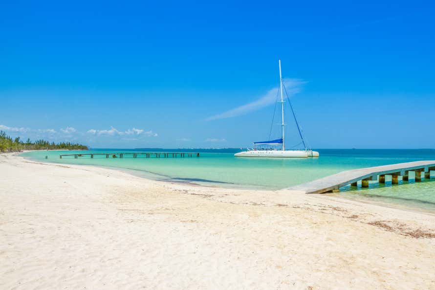 Praia de Varadero vazia com uma faixa de areia clara e uma embarcação nas águas de tom esverdeado em um dia de sol