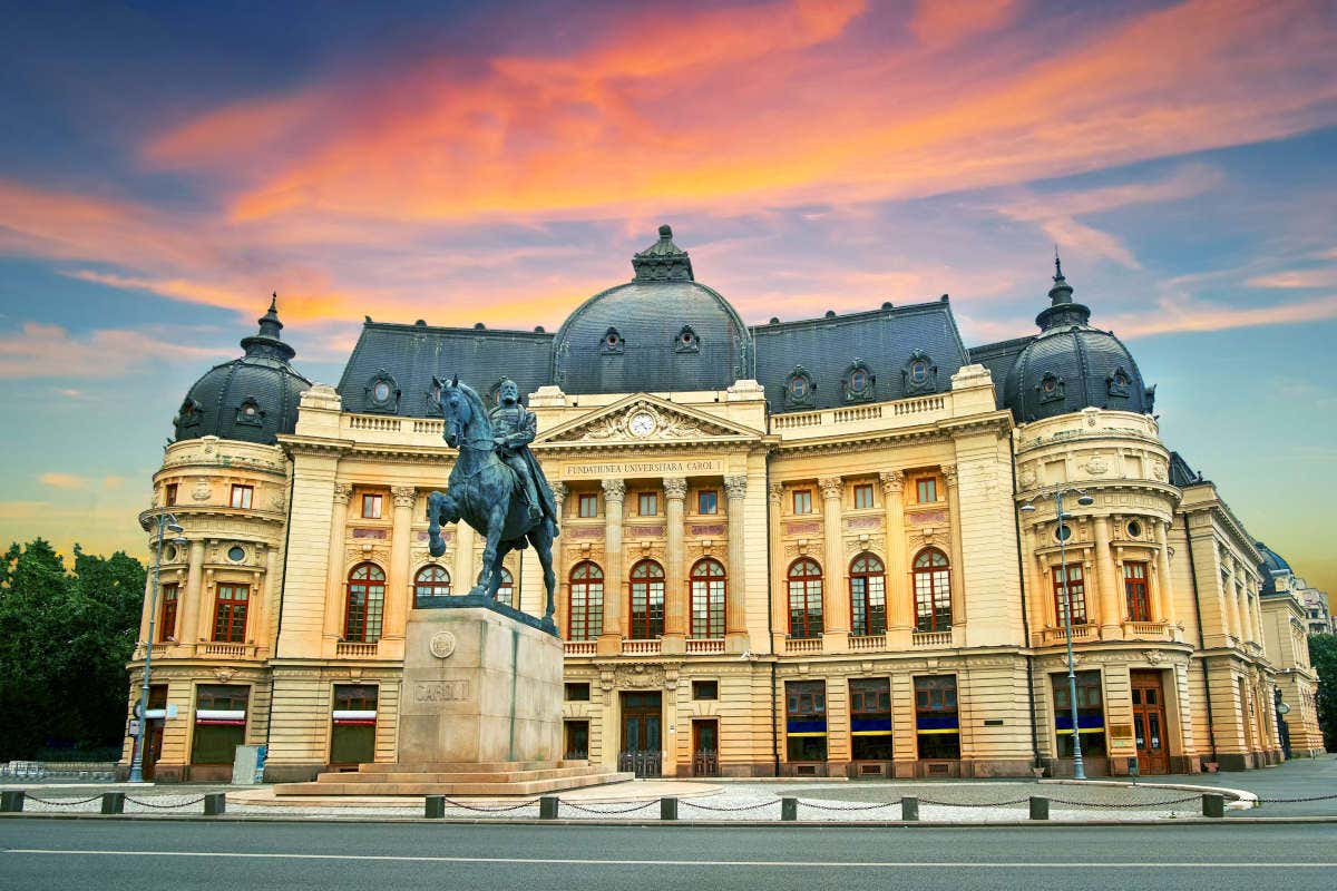 Façade de la Bibliothèque nationale de Bucarest au coucher du soleil avec la statue d'un cavalier devant
