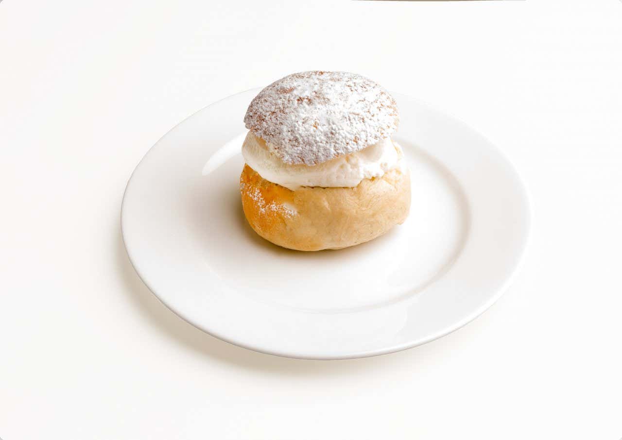 A traditional icelanding bun topped with icing sugar on a white plate.