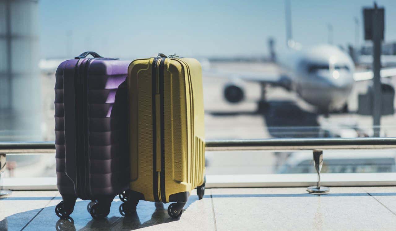 Dos maletas de mano en los pasillos de un aeropuerto, con un avión al fondo de la imagen.