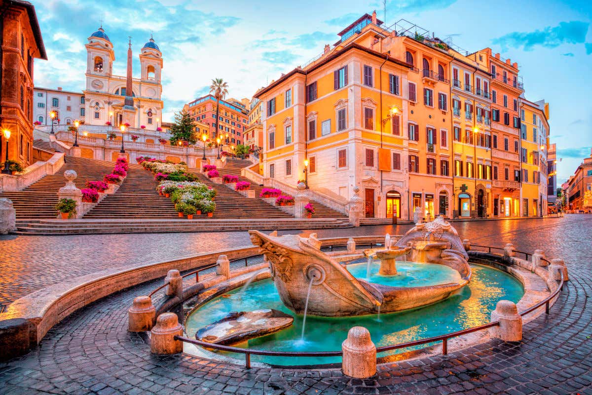 Sunset over the Spanish Steps in Rome, with the lampposts on and the steps decorated with pink azaleas.