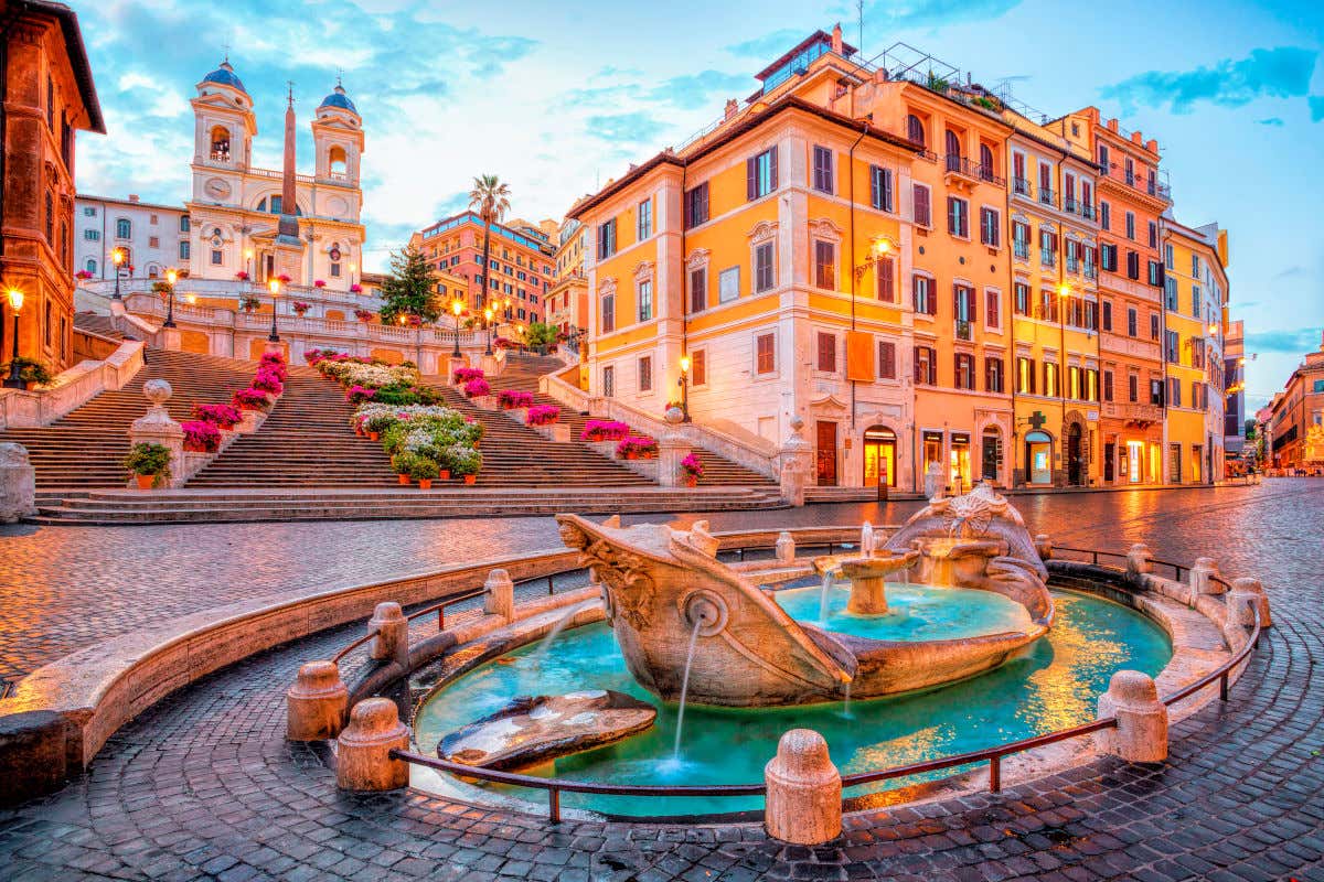 Atardecer en la plaza España de Roma, con las farolas iluminadas y las escalinatas decoradas con flores azaleas rosas.