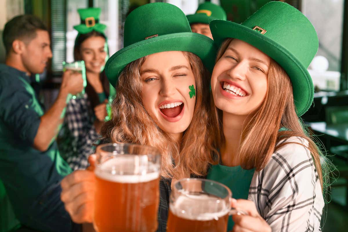 Deux femmes avec des pintes de bière souriant pour la photo et parées de chapeaux haut-de-formes verts pour célébrer le jour de la Saint-Patrick dans un pub