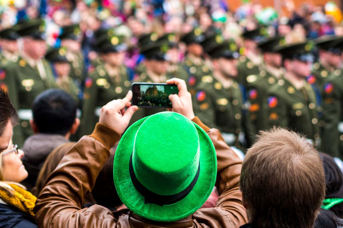 Un homme avec un chapeau vert dans une foule de personnes et prenant une photo avec son portable lors du défilé du jour de la Saint-Patrick à Dublin