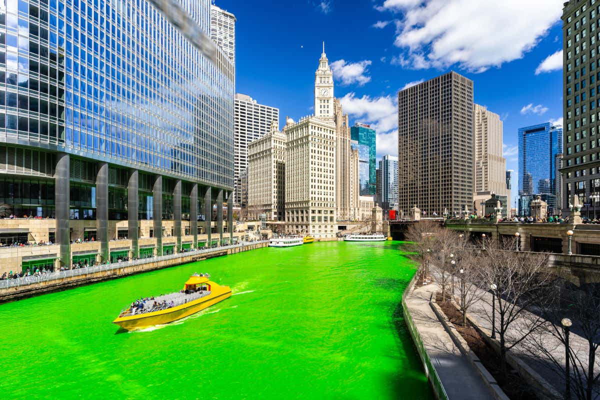Un bateau naviguant dans une rivière verte passant entre les gratte-ciels de Chicago le jour de la Saint-Patrick