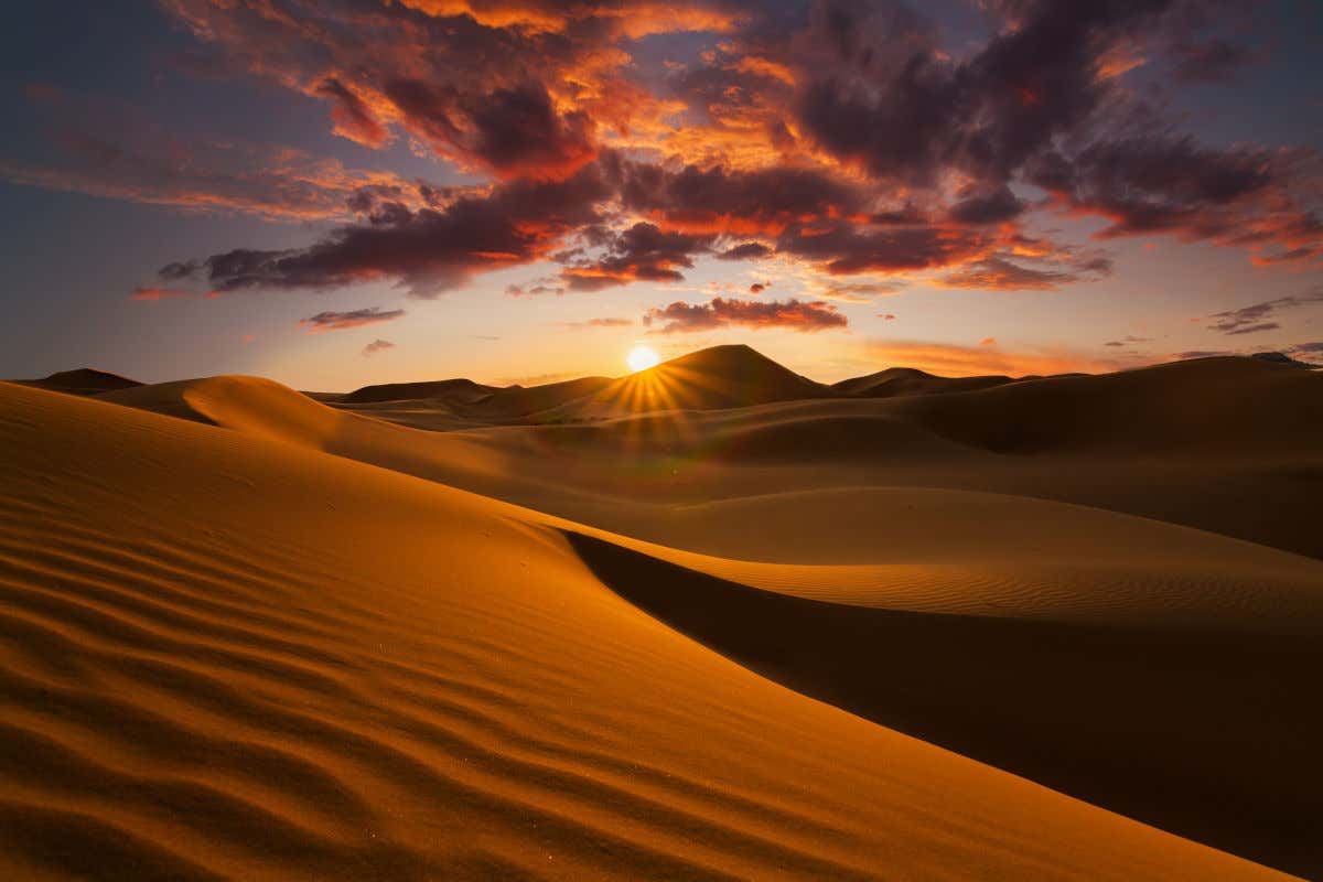 Dunas de areia dourada sem pessoas nem animais caminhando sobre elas destacam um dia parcialmente nublado antes do amanhecer no deserto do Saara