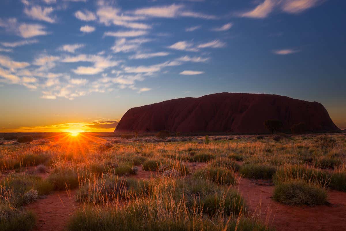 Uluru, a rocha sagrada do desierto da Austrália, ao amanhecer em um dia com poucas nuvens