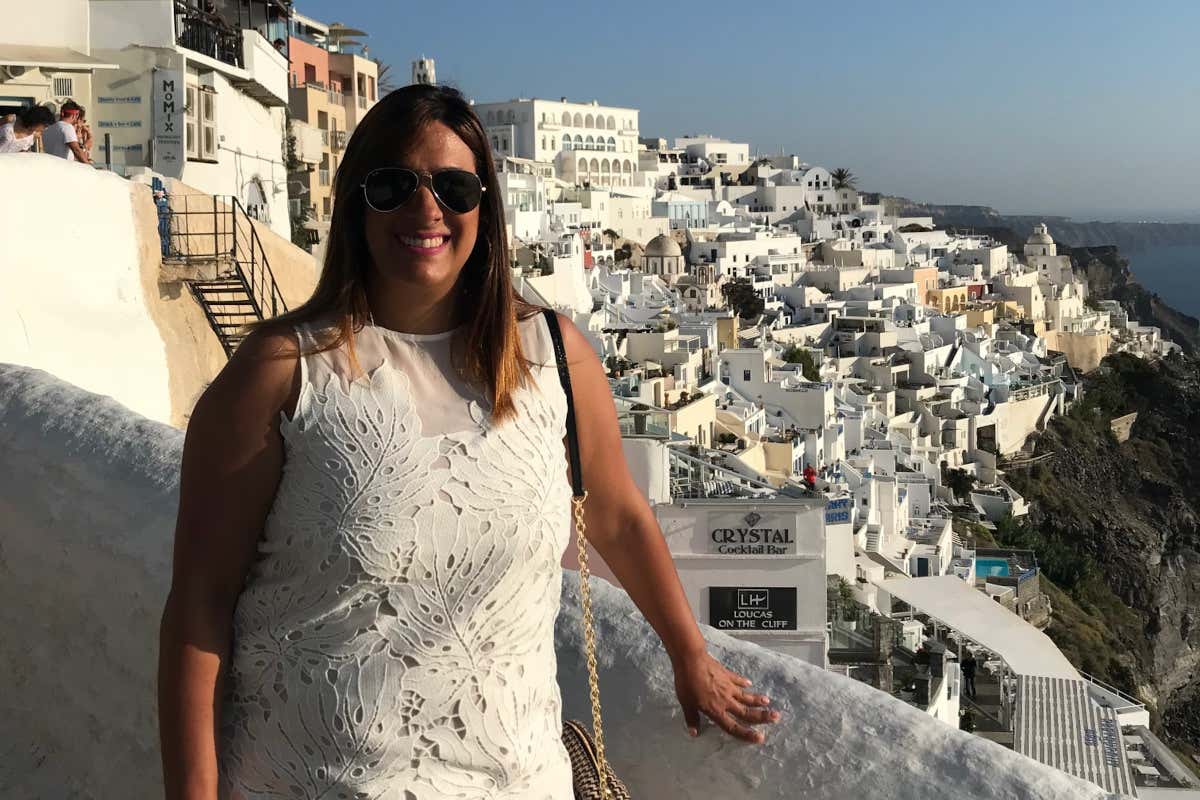 Laura Ferández vestida con un traje blanco en un mirador de la isla de Santorini, desde donde se pueden ver muchas casas blancas y restaurantes.