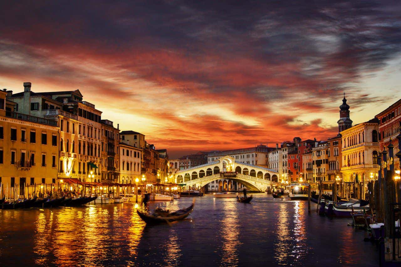 Pont du Rialto au coucher du soleil entouré de bâtiments illuminés avec des gondoles passant en dessous
