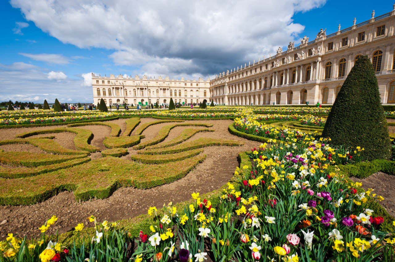 Flores coloridas com o Palácio de Versalhes de fundo, um dos palácios mais bonitos do mundo
