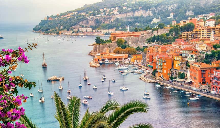 An aerial view of Villefranche-sur-Mer, with numerous boats in the bay and colourful orange buildings along the water