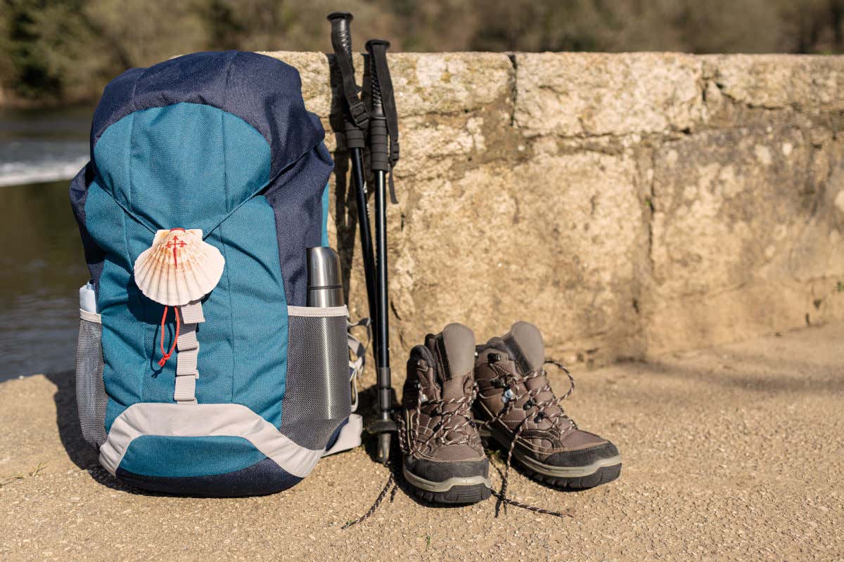 Un sac à dos, un bâton de marche, une croix de Saint-Jacques et des chaussures de sport, près d'une rivière.