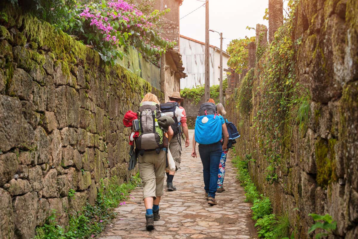 Quatre pèlerins avec leurs sacs à dos marchant dans les rues pavées d'un village sur le Chemin de Saint-Jacques.
