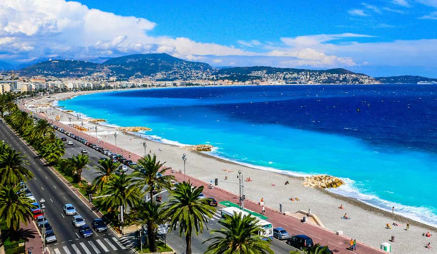 An aerial view of the coastline of Nice, with palm trees lining the coastal road and clouds visible in the sky