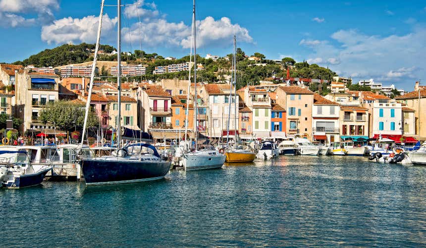 The Port of Cassis, with numerous boats moored in the dock in front of colourful buildings and a view of a hill in the background