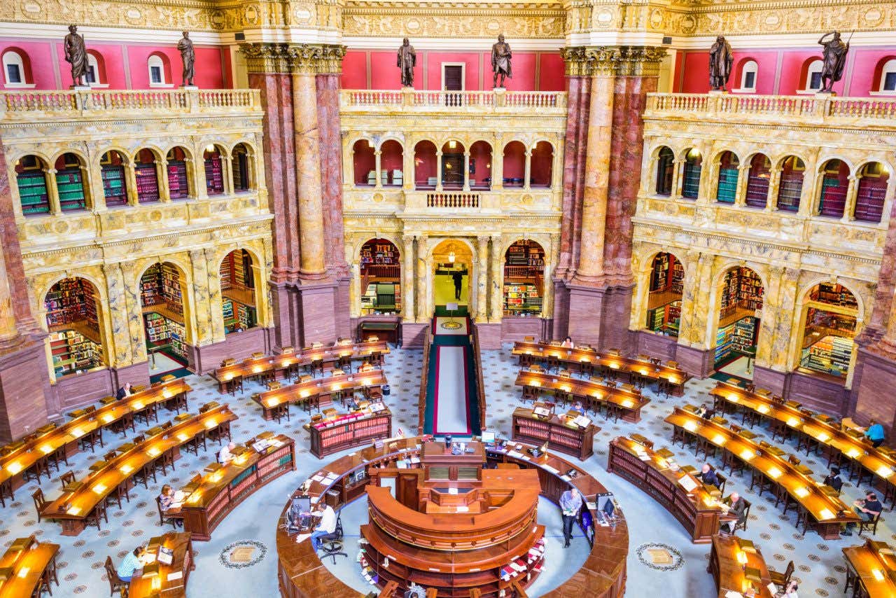 The Library of Congress in the US Capitol building with desks lit up with lamps and a few people sat at them
