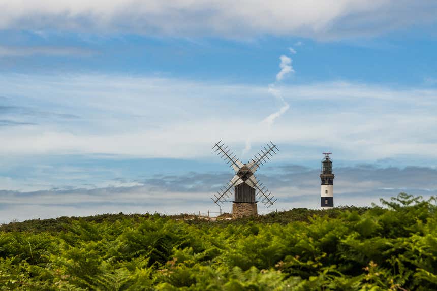 O Farol de Creach ao lado de um moinho de vento, ambos entre a vegetação da ilha