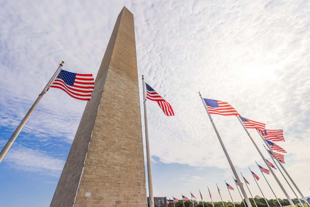The towering Washington Monument, surrounded by United States flags against a cloudy sky