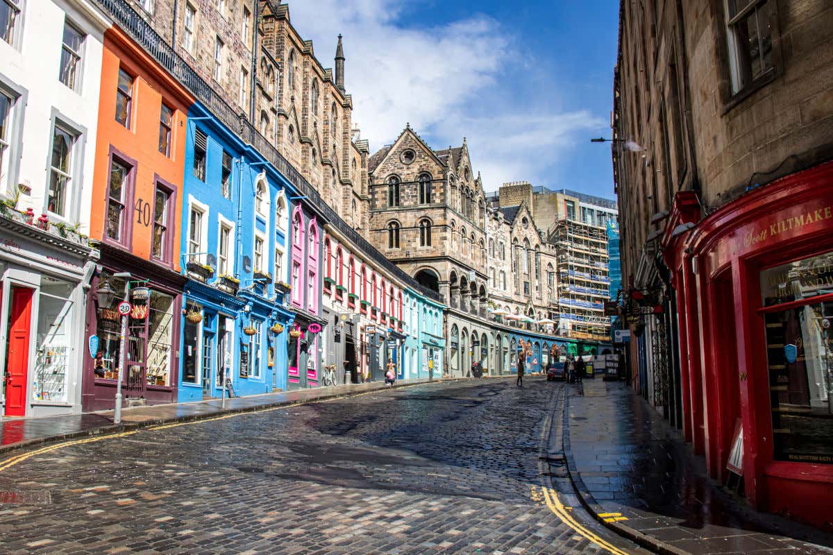 Fachadas coloridas das lojas da Victoria Street de Edimburgo em um dia de sol. No fim da rua há edifícios em reforma