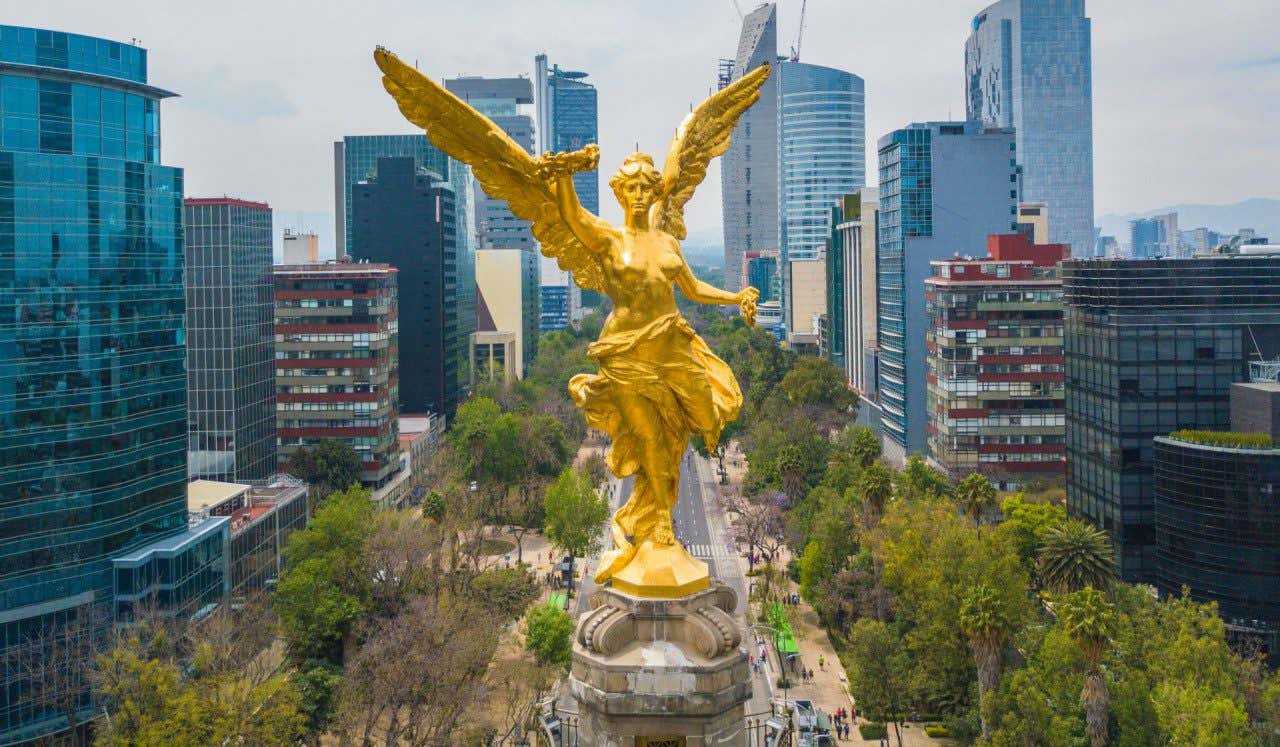 Escultura dorada del Ángel de la Independencia ubicado en el Paseo de la Reforma de Ciudad de México frente a modernos edificios