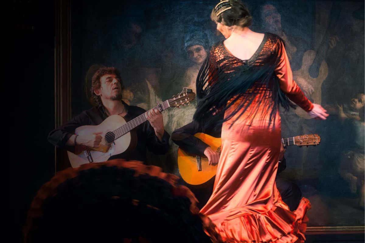 Une danseuse de flamenco avec une robe rouge près de deux guitaristes sur la scène de el Corral de la Morería à Madrid