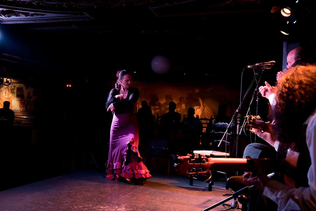 Une danseuse de flamenco près d'un groupe de musiciens sous la lumière tamiséé du Tablao Flamenco 1911 de Madrid