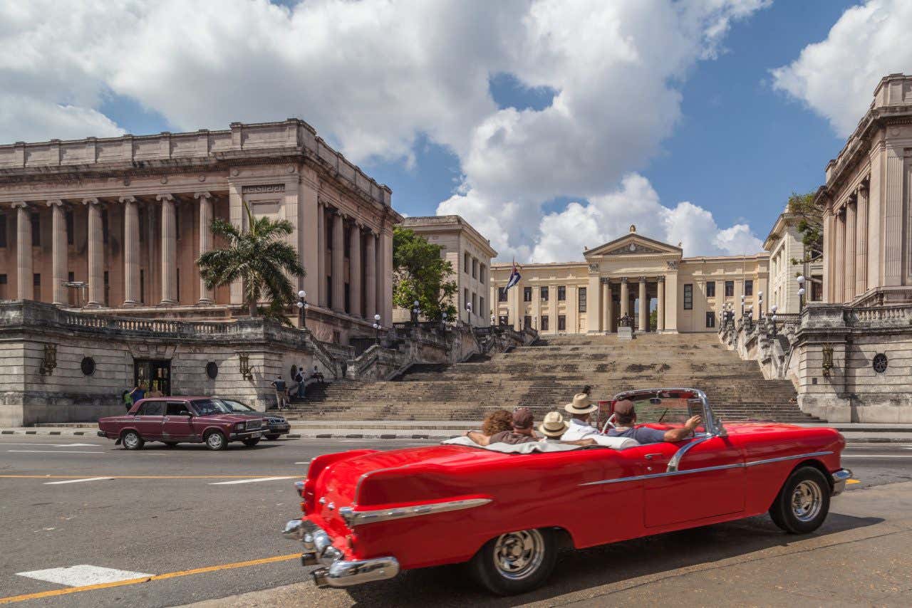Um carro clássivo vermelho diante da fachada da Universidade de Havana