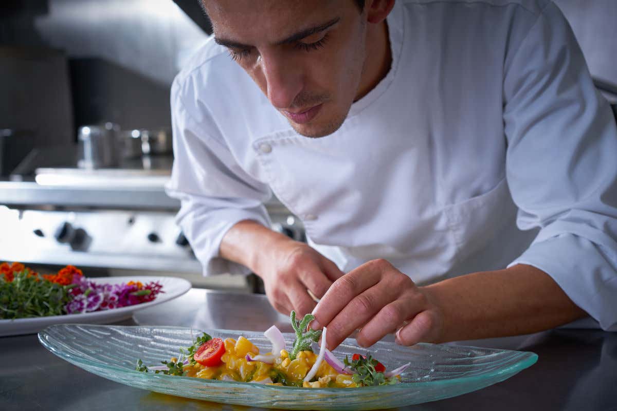 Un chef con chaquetilla blanca preparando un plato de ceviche en una cocina profesional