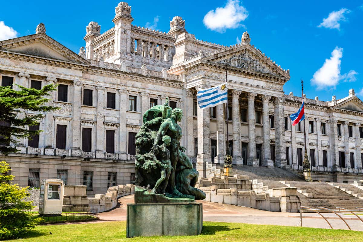 Front view of the Parliament of Uruguay in Montevideo decorated with two flags and a sculptural ensemble next to entrance