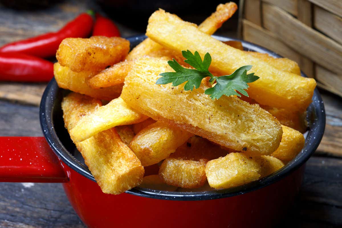 A small decorative red casserole dish with a garnish of fried cassava