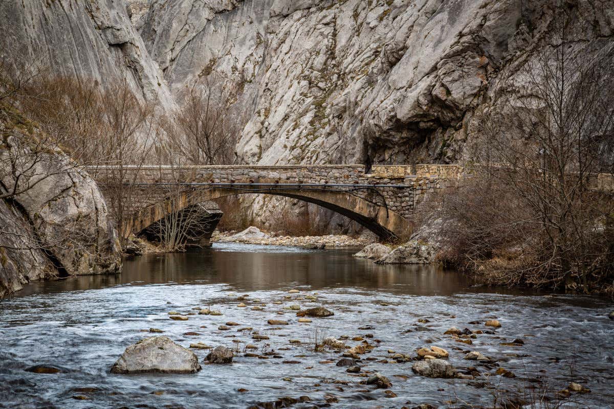 Un puente de piedra se alza sobre un río rodeado por altas montañas en el paraje natural de Hoces de Vegacervera