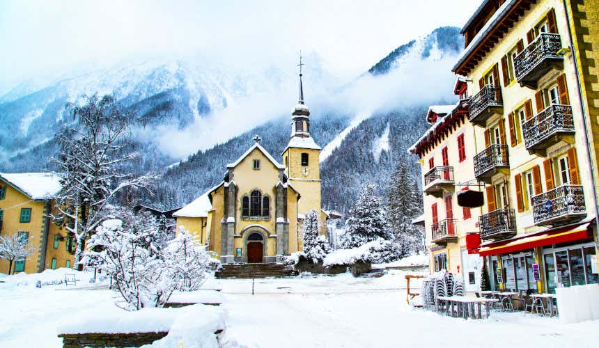 Igreja de Chamonix-Mont-Blanc com as montanhas nevadas atrás e uma paisagem cheia de neve nas ruas
