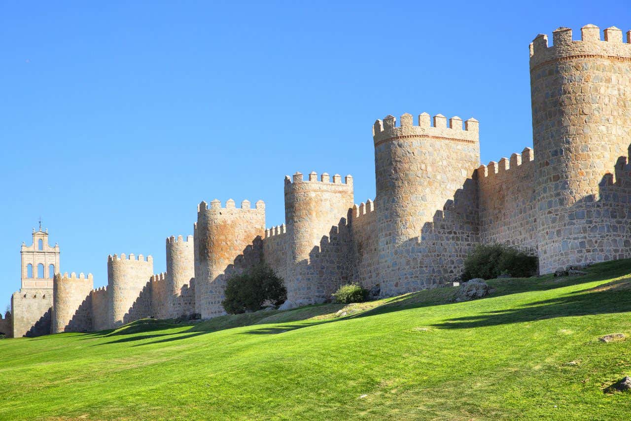Muralla de Ávila un día soleado con el cielo azul de fondo y el césped de color verde