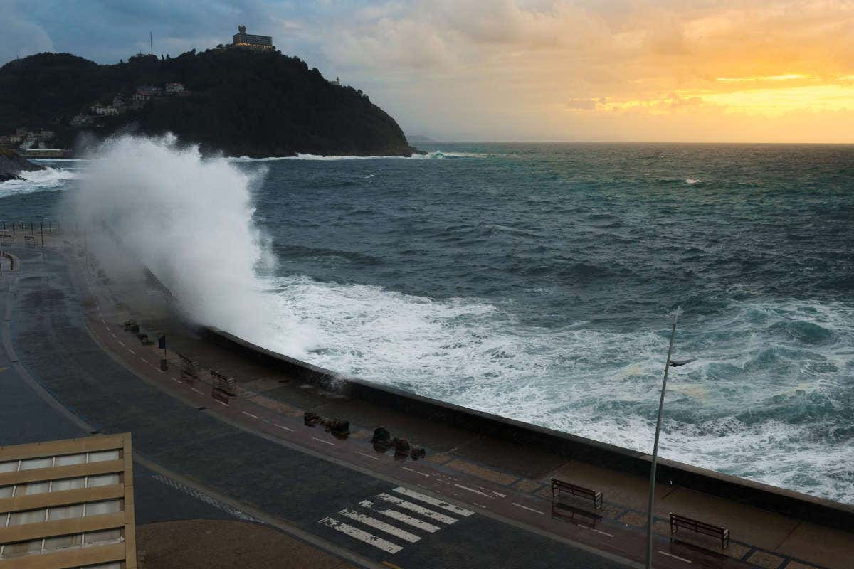 Sunset in San Sebastián and a strong wave breaking against the promenade and rising up onto the pavement, cliffs in the background