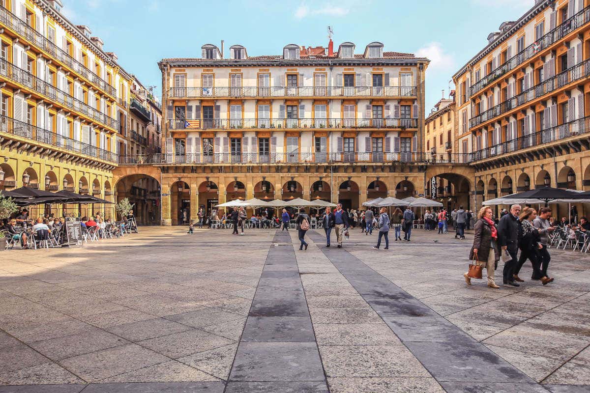 View of the arcades of the Plaza de la Constitución with people passing by and eating in terraces