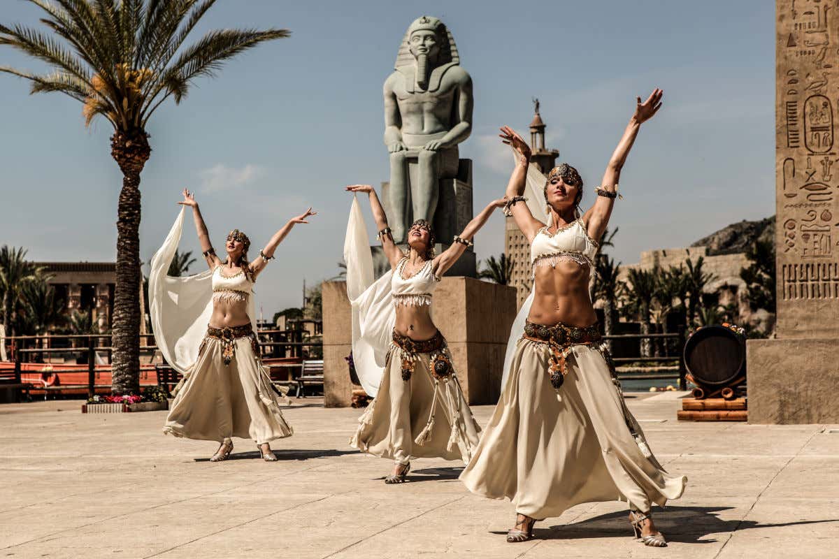 Tres bailarinas ataviadas con disfraces del Antiguo Egipto frente a una escultura en el parque temático de Terra Mítica, en Benidorm