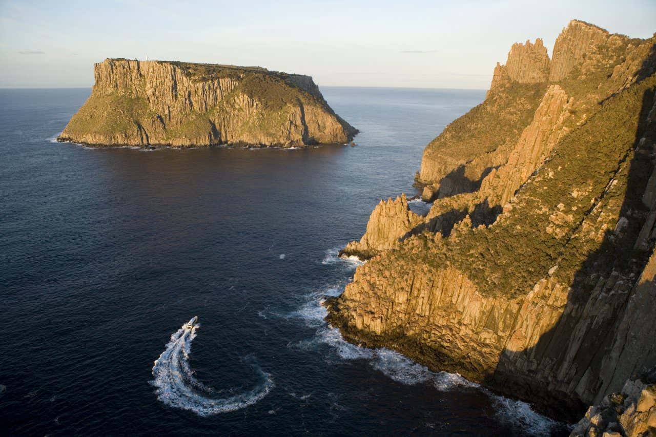 Vue sur la côte écharpée de l'île de Tasmanie avec un bateau naviguant près des falaises