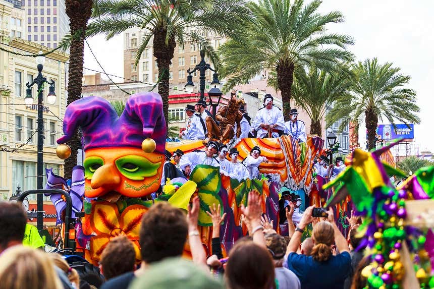 People dressed up in masks and hats on a float traveling down a crowded street