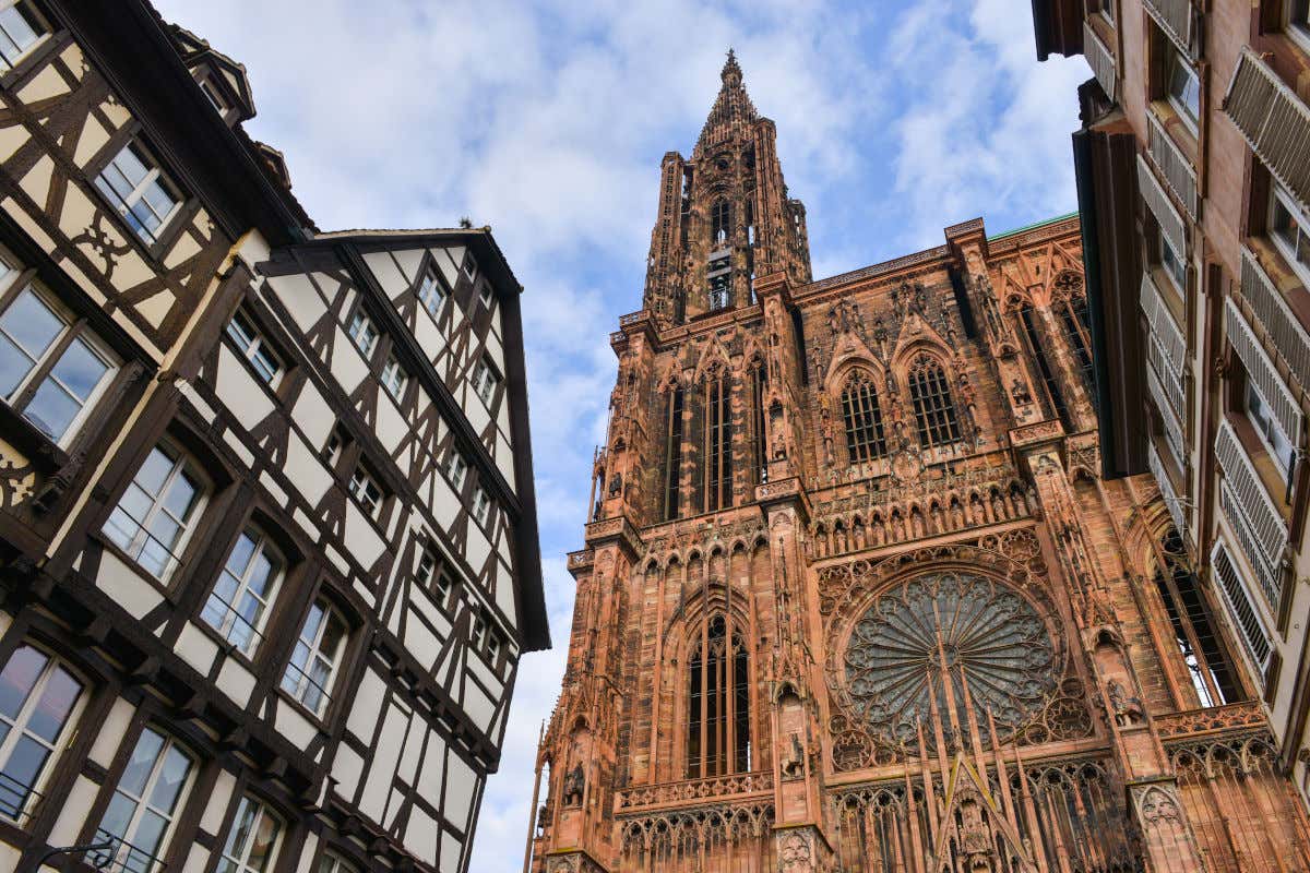 Fachada frontal de la catedral de Estrasburgo entre dos casas típicamente alsacianas en un día parcialmente despejado
