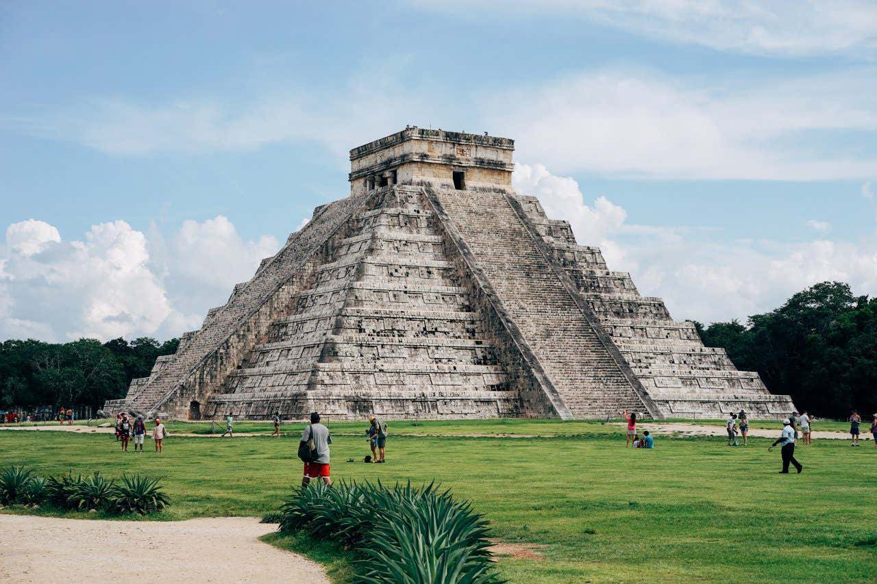 The Maya Pyramid at Chichén Itzá with people strolling around the grass outside of it in Mexico