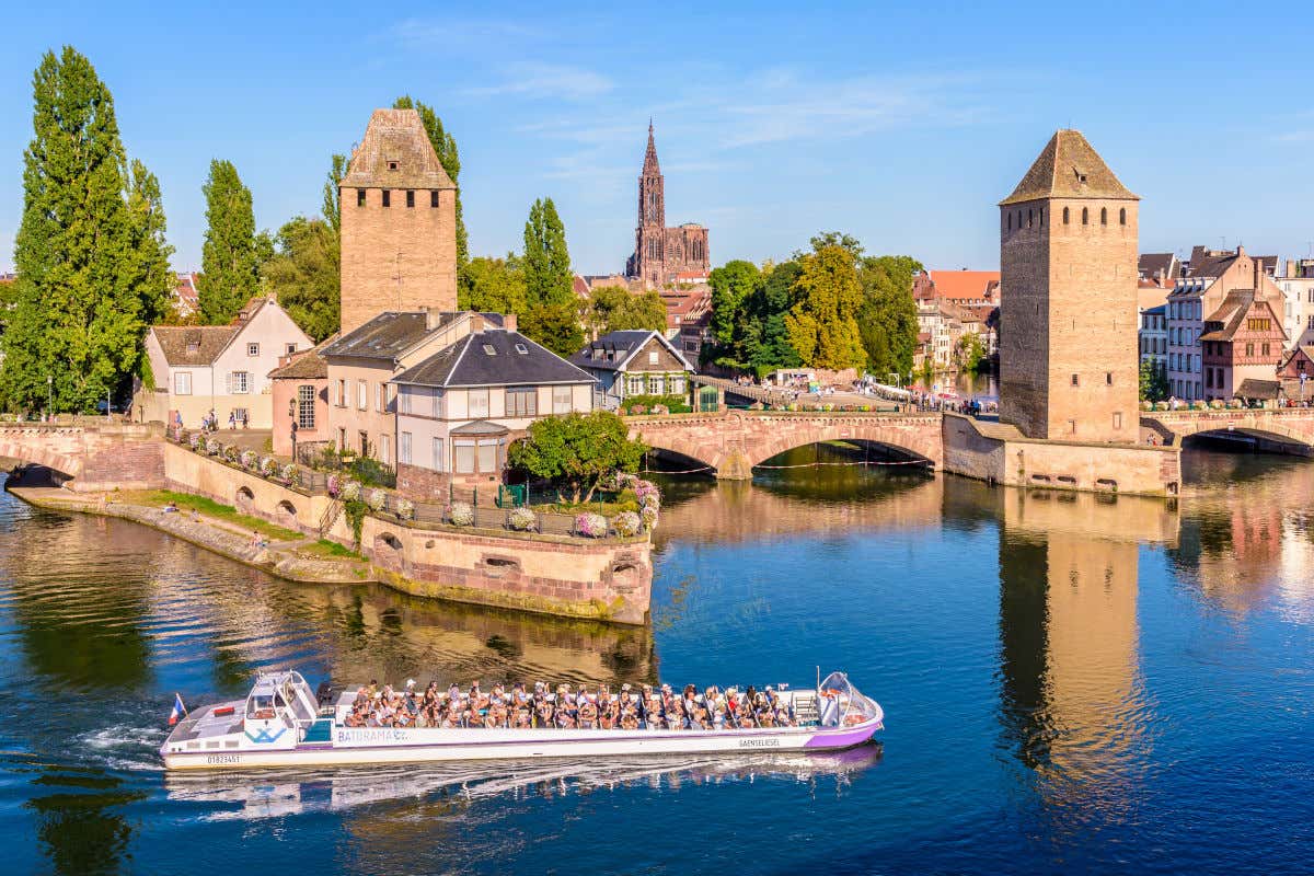 Un barco navegando por Estrasburgo frente a las torres defensivas de los puentes cubiertos y la Catedral al fondo