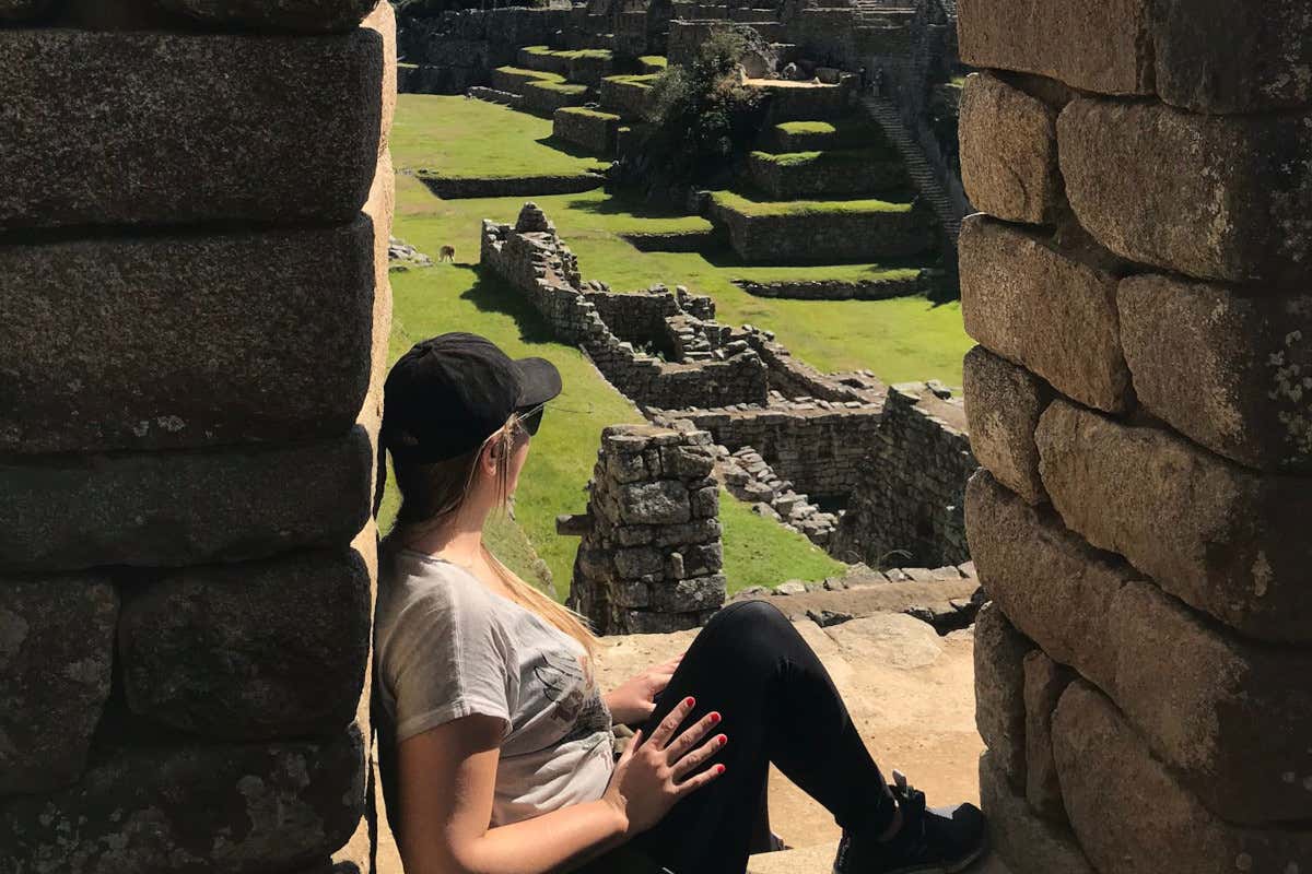 Romina Biggo sentada entre dos muros contemplando las ruinas de Machu Pichu