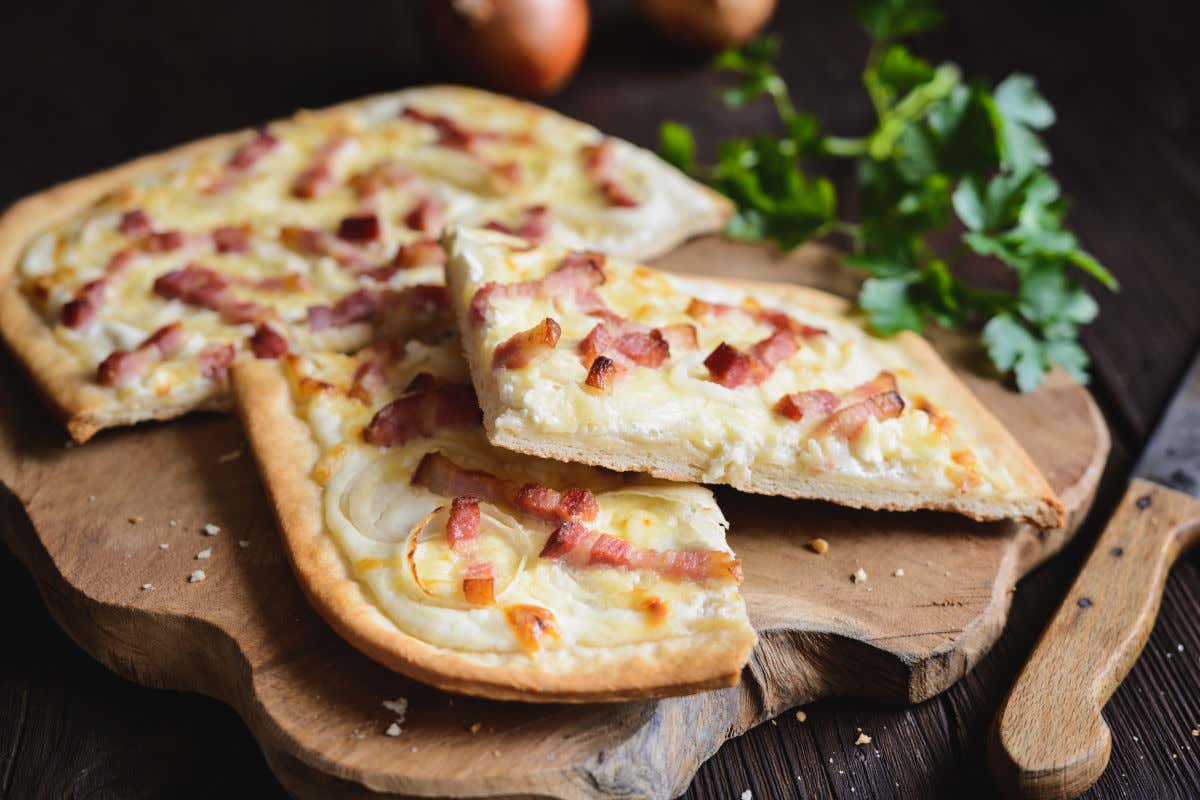 Uma tábua de madeira com uma tarte flambée assada com bacon, cebola e creme de leite