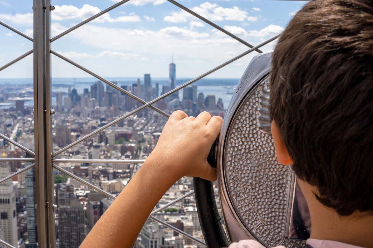 A boy with his back to the camera using one of the telescopes on the observation deck of the Empire State Building in New York.