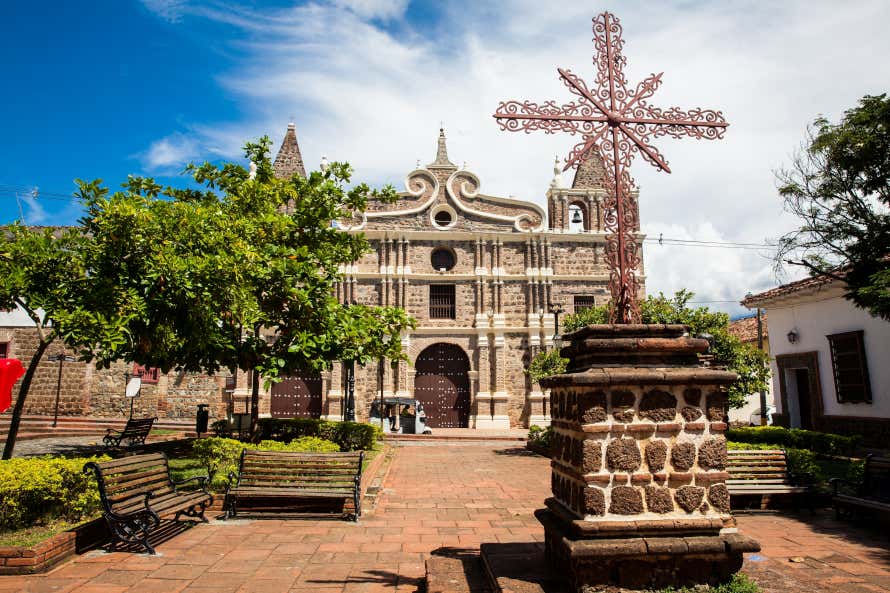 Facciata della chiesa e piazza antistante con panchine e croce metallica nel centro a Santa Fe de Antioquia