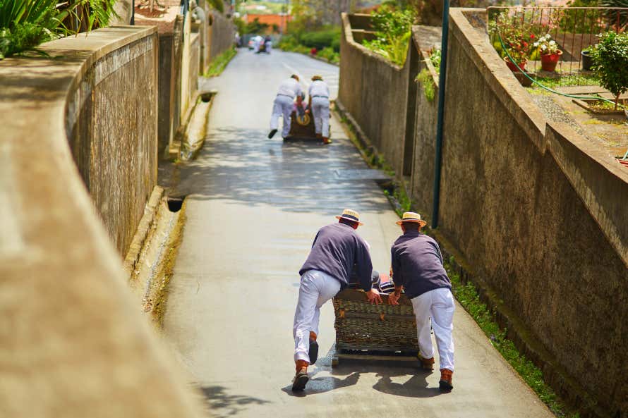 Carreiros pushing wicker basket sledges a sloping street in Monte.