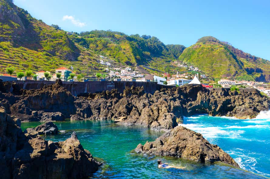 Acantilados y piscinas naturales de Porto Moniz frente a un grupo de montañas verdes de Madeira 